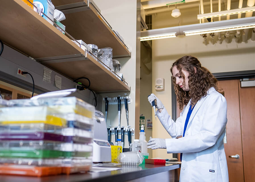 Student in white lab coat working in a biology lab.