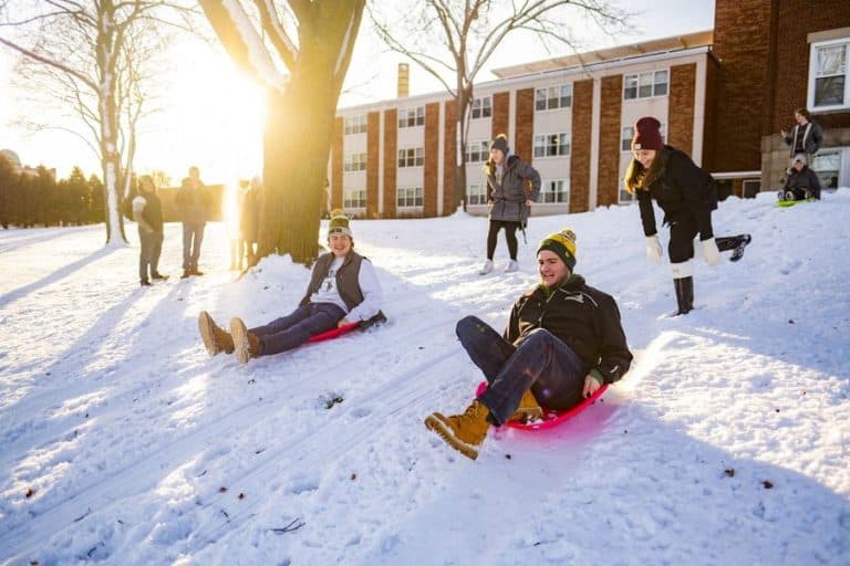 SNC students riding sleds down a snowy hill on campus